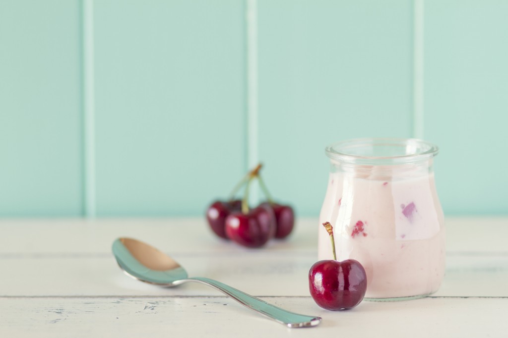 A jar with cherry yogurt and some cherries in a white wooden table with a robin egg blue background. Vintage style.