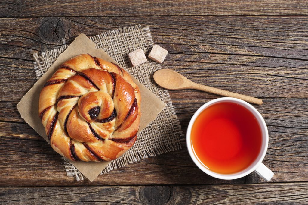 Cup of hot tea and sweet bun with jam on old wooden table, top view