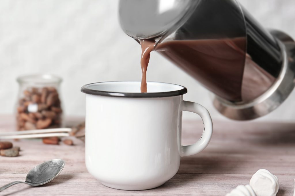 Pouring hot cocoa drink into metal mug on kitchen table
