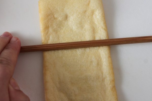 薄揚げをまな板に置き、さいばし等で上からコロコロと少し力を入れて転がす(こうすると、中がはがれやすくなります)。