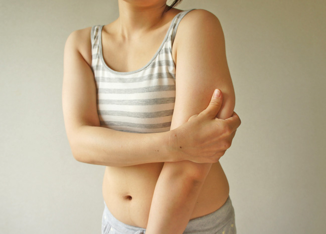 二の腕をつまむ女性