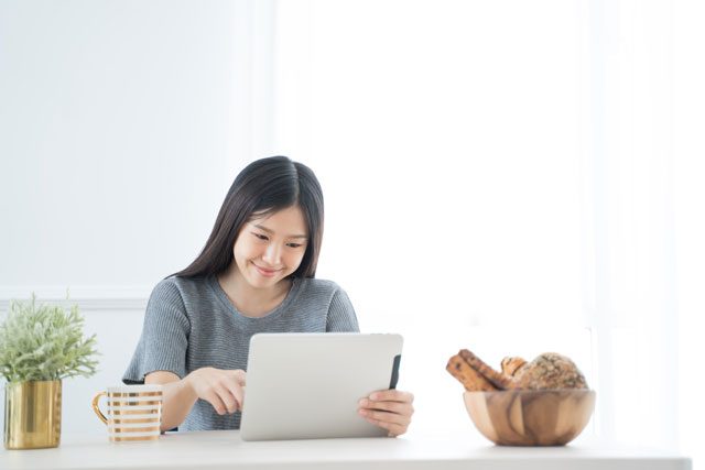 朝のテーブルでタブレットを操作する女性
