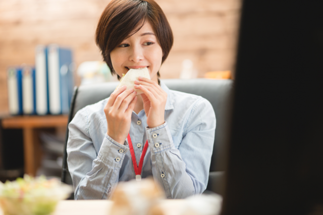 デスクでサンドイッチ食べる女