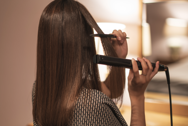 髪にヘアアイロンをあてる女性